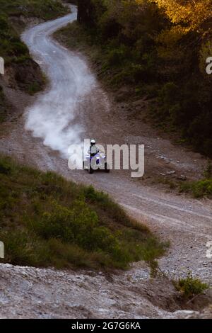 Mann auf dem blauen ATV Quad auf der Offroad-Strecke in den Bergen, die viel Staub aufwirbelt Stockfoto