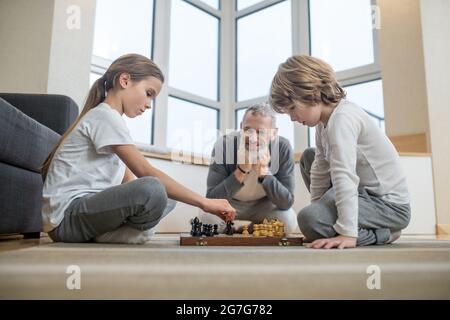 Geschwister spielen Schach, während ihr Vater zuschaut Stockfoto