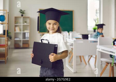 Portrait von glücklichen hübschen kleinen Studenten Mädchen in akademischen Mütze im Klassenzimmer stehen Stockfoto