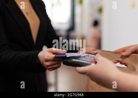 Nahaufnahme einer Geschäftsfrau, die eine Plastikkreditkarte in der Hand hält und im Büro des Unternehmens für die Lieferung von Lebensmitteln bezahlt. Mit kontaktlosem Pay für Essen zum Mitnehmen. . Bringen Sie leckeres Essen mit. Stockfoto