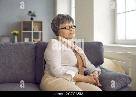 Porträt einer glücklichen älteren Frau im Ruhestand, die zu Hause auf der Couch sitzt und wegschaut Stockfoto
