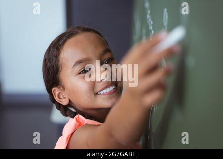 Porträt einer Schülerin mit gemischter Rasse, die auf einer Tafel im Klassenzimmer steht Stockfoto