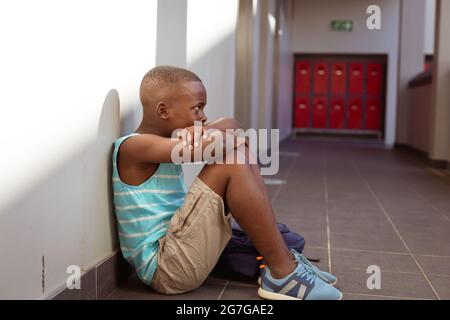 Verärgert afroamerikanischen Schuljungen sitzen auf dem Boden in der Schule Korridor Stockfoto