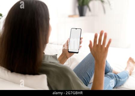Indische Frau hält und nutzt Smartphone mit schwarzem leeren Bildschirm für die Videoverbindung, winkt Hallo in die Webcam, mit der neuen mobilen App für virtuelle Meetings. Mockup, Kopierfläche für Werbung Stockfoto