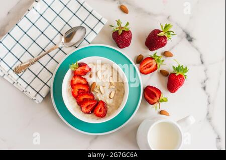 Haferflocken Haferbrei mit Erdbeeren und Mandeln in einer weißen Schüssel. Gesundes Frühstück mit Haferflocken und frischen Bio-Beeren Stockfoto