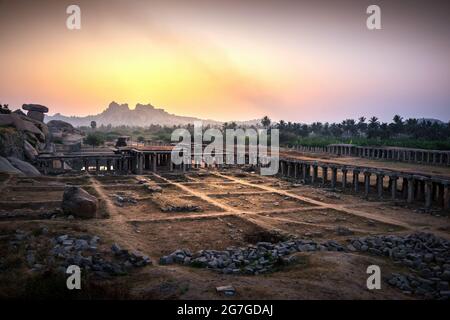 Blick auf Sonnenaufgang in Pushkarni, Sri Krishna Tank in Ruinen. südseite des Pools mit Schrein. Felsbrocken und Berge am Horizont. Hampi, Karnataka, Indien. Stockfoto