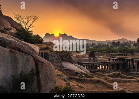 Blick auf Sonnenaufgang in Pushkarni, Sri Krishna Tank in Ruinen. südseite des Pools mit Schrein. Felsbrocken und Berge am Horizont. Hampi, Karnataka, Indien. Stockfoto