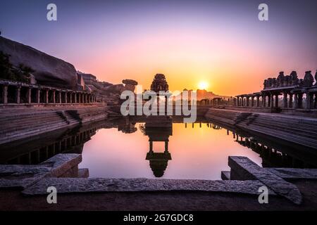 Blick auf Sonnenaufgang in Pushkarni, Sri Krishna Tank in Ruinen. südseite des Pools mit Schrein. Felsbrocken und Berge am Horizont. Hampi, Karnataka, Indien. Stockfoto