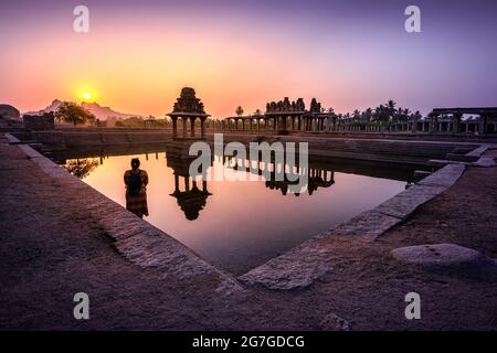 Blick auf Sonnenaufgang in Pushkarni, Sri Krishna Tank in Ruinen. südseite des Pools mit Schrein. Felsbrocken und Berge am Horizont. Hampi, Karnataka, Indien. Stockfoto