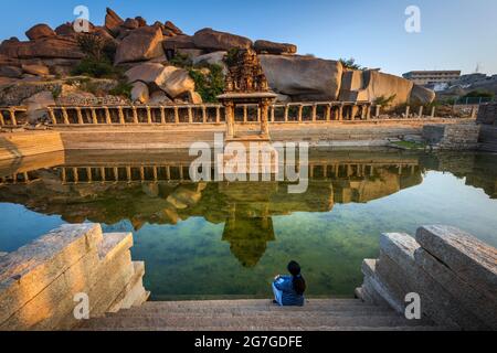 Blick auf Sonnenaufgang in Pushkarni, Sri Krishna Tank in Ruinen. südseite des Pools mit Schrein. Felsbrocken und Berge am Horizont. Hampi, Karnataka, Indien. Stockfoto