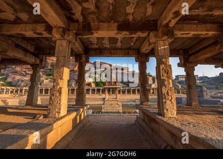 Blick auf Sonnenaufgang in Pushkarni, Sri Krishna Tank in Ruinen. südseite des Pools mit Schrein. Felsbrocken und Berge am Horizont. Hampi, Karnataka, Indien. Stockfoto