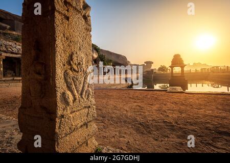 Blick auf Sonnenaufgang in Pushkarni, Sri Krishna Tank in Ruinen. südseite des Pools mit Schrein. Felsbrocken und Berge am Horizont. Hampi, Karnataka, Indien. Stockfoto