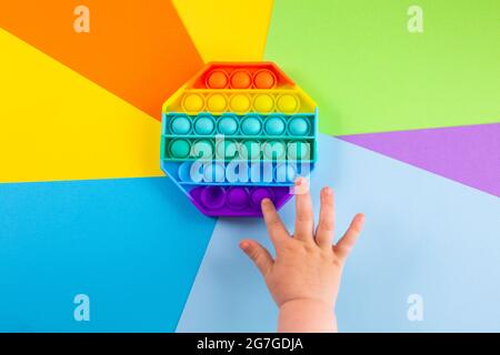 Kinder Hände schieben sensorische popit auf bunten Hintergrund. Antistress-Pop-it-Spielzeug. Rainbow Silikon sensorische Fidget Neue beliebte trendige Silikon-Spielzeug. Stockfoto