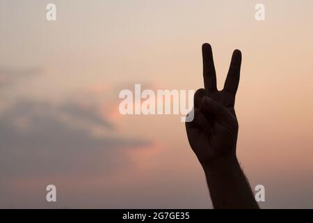 Mann, der das Friedenssymbol mit der Hand gegen den Abendhimmel kreist - Silhouette Stockfoto