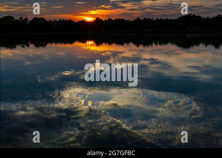 Der Sonnenuntergang spiegelt sich im Wasser eines ländlichen Sees wider Stockfoto