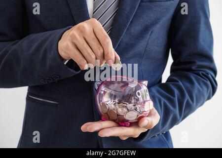 Geschäftsmann, der Münzen in Sparschwein-, Finanz- und Investitionskonzept einbringt. Stockfoto