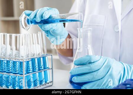 Biochemische Laborforschung, Wissenschaftler oder Mediziner in Laborkittel, der Reagenzglas mit einem Tropfen Farbflüssigkeit über Glasgeräte hält Stockfoto