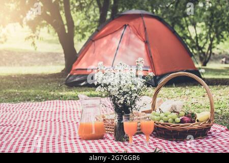 Gesunde Ernährung und Zubehör outdoor Sommer oder Frühling Picknick Picknick Weidenkorb mit frischem Obst, Brot und ein Glas frischen Orangensaft in t Stockfoto