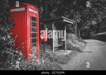 Traditionelle rote britische Telefonzelle, Briefkasten und hölzerne Bushaltestelle, selektive Farbe auf schwarzem und weißem Hintergrund, keine Menschen. Wales, Großbritannien Stockfoto