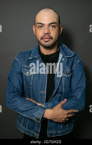 Porträt eines jungen hübschen mexikanischen Glatzenmanns, der eine Denim-Jacke auf einem grauen Hintergrund trägt Stockfoto