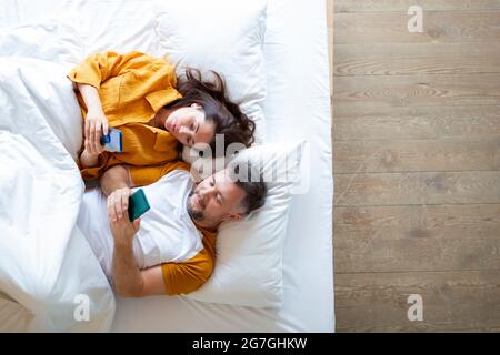 Draufsicht auf das lebende Paar, das mit Smartphones im Bett liegt. Konzept moderner Technologien im Alltag. Stockfoto