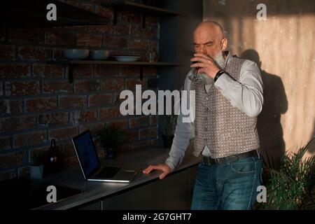 Geschäftsmann mit einem Glas Wein auf den Bildschirm seines Laptops schauen. Stockfoto