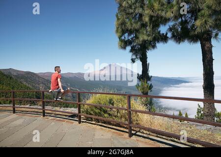 Mann, der auf dem Geländer sitzt und auf die wunderschöne Landschaft über den Wolken gegen den Pico de Teide blickt. Teneriffa, Kanarische Inseln, Spanien. Stockfoto