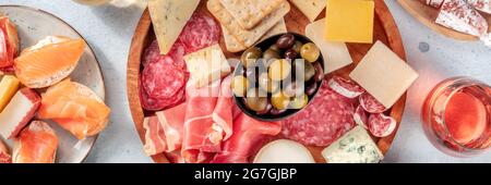 Panorama von Aufschnitt und Käseplatte mit Rosenwein und Lachs-Sandwiches, Top Shot. Ein Panorama-Banner für ein italienisches Antipasti-Restaurant-Menü. Prosciutto di Parma, Salami, Blauschimmelkäse Stockfoto