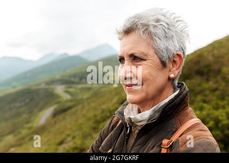 Positive ältere weibliche Reisende Gesicht und Blick weg auf verschwommenen Hintergrund der Natur Stockfoto