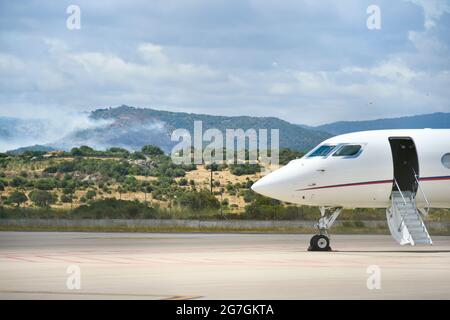 Blick auf ein Feuer in der Nähe des Flughafens Olbia Costa Smeralda mit Flugzeugen, die auf der Start- und Landebahn abgestellt sind Stockfoto