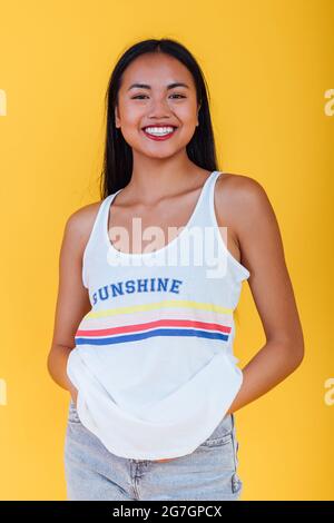 Entzückte asiatische Frau, die auf gelbem Hintergrund im Studio steht, während sie die Kamera anschaut Stockfoto