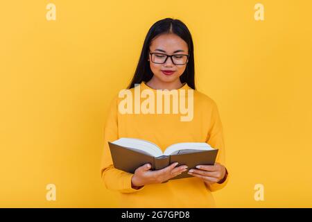 Clever asiatische Studentin in Brillen Lehrbuch lesen und Vorbereitung auf die Prüfung auf gelbem Hintergrund im Studio Stockfoto