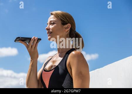 Junge Frau, die sich auf ihrem Smartphone unterhielt, während sie sich vom Training im Freien ausruhte und lächelte Stockfoto