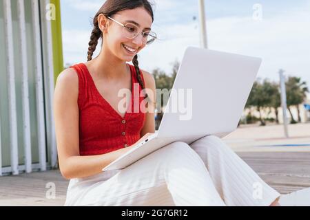 Content Freiberuflerin sitzt am Meer und tippt auf dem Laptop, während sie im Sommer an einem Projekt aus der Ferne arbeitet Stockfoto
