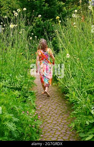 Frau in einem bunten Sommerkleid, die durch ein Blumenbett geht, Deutschland Stockfoto