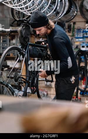 Seitenansicht des jungen erfahrenen männlichen Mechanikers mit Werkzeug Montage Kettenrad auf Fahrrad während der Reparatur Service-Arbeiten in der Werkstatt Stockfoto