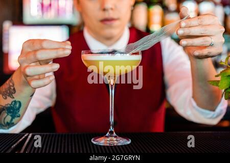 Anonyme, professionelle junge Barkeeperin, die mit einer Feder dekoriert, während sie in der Bar sauren Cocktail zubereitet Stockfoto
