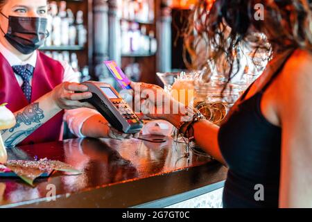 Barkeeperin mit POS-Terminal am Tresen stehend, mit einer anonymen Frau, die mit Plastikkarte für die Bestellung in der Bar bezahlt Stockfoto