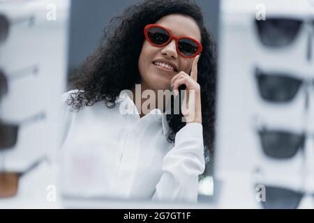 Nahaufnahme. Lächelnde junge Frau, die in einem Optometrie-Geschäft eine Sonnenbrille anprobiert. Stockfoto