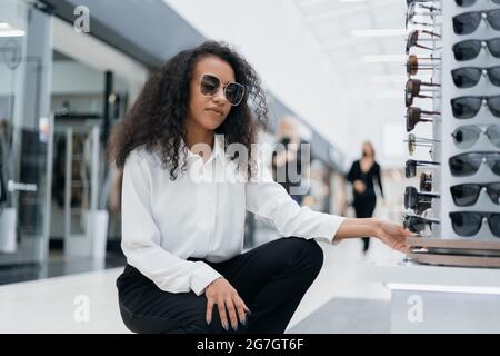 Junge Frau, die in der Optometrie-Abteilung auf die Brille auf dem Tresen schaut. Stockfoto