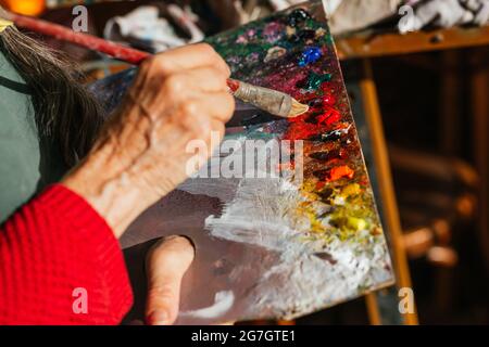 Von oben der Ernte unkenntlich ältere weibliche Malerin mischen Farben auf Farbpalette in der Kunstwerkstatt Stockfoto