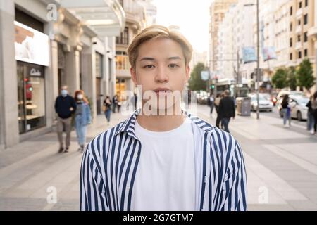 Trendiges asiatisches männliches Modell mit blondem Haar, das in der Stadtstraße steht und die Kamera anschaut Stockfoto