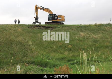 EINGEREICHT - 14. Juli 2021, Sachsen-Anhalt, Sandau: Ein Bagger steht vor dem Spatenstich für den Deichschlitz auf dem alten Deich Sandau-Süd. Die vergangenen Hochwasserereignisse in den Jahren 2002 und 2013 zeigten, dass der bestehende Deich zwischen Sandau und Havelberg dringend saniert werden muss. Die Deichumsiedlung ist Teil des Nationalen Hochwasserschutzprogramms der Bundesrepublik Deutschland und des Programms "Mehr Raum für unsere Flüsse" in Sachsen-Anhalt. Durch den Umzug werden hier rund 124 Hektar Auengebiet zurückgewinnen, im Vergleich zu rund 60 Hektar für das Sandau-Nord-Bauprojekt. Stockfoto