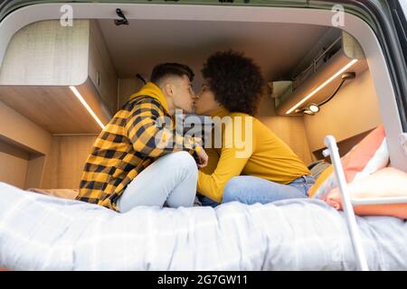 Seitenansicht von verschiedenen Männern und Frauen, die sich gegenseitig küssen, während sie auf dem Bett in einem modernen Van auf der Straße sitzen Stockfoto