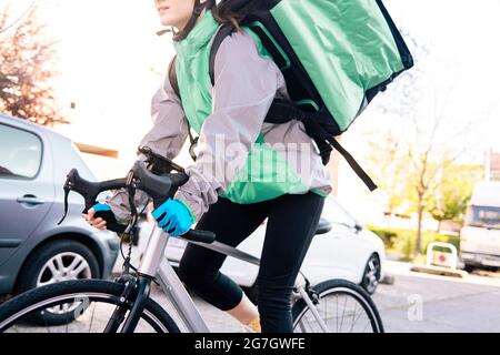 Low-Angle-Ernte der weiblichen Kurierin mit Thermal-Tasche Fahrrad auf der Straße fahren, während die Lieferung an sonnigen Tag in der Stadt Stockfoto