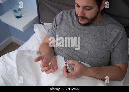Junger latein erkrankt im Bett und nimmt eine Pille. Gefühl krank Konzept. Stockfoto