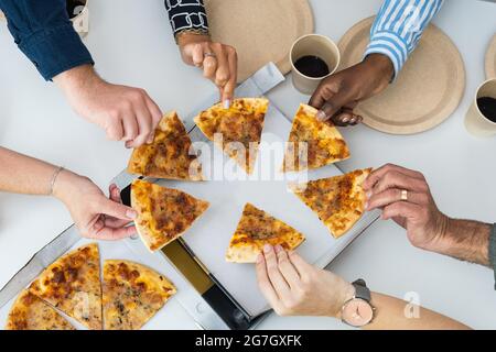 Von oben Gesellschaft der Ernte anonymen multiethnischen Freunde versammeln sich am Tisch und essen leckere Pizza Stockfoto