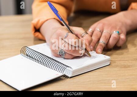 Freiberufliche Mitarbeiterin beim Schreiben auf Notizblock, während sie mit einem Laptop im Café am Tisch sitzt und an einem Remote-Projekt arbeitet Stockfoto