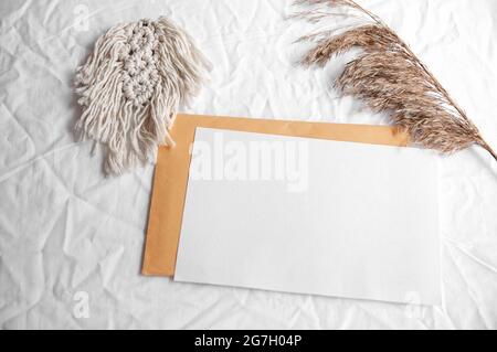 Umschlag, Macrame, Pampagras. Einfache minimale flache Lage auf weißem Textil mit trockener Erdfarbe neutrales Beige mit Macrame und trockenem Schilf, Pampagras. Stockfoto