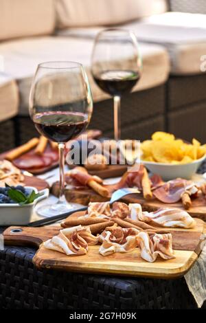 Köstlicher Speck auf Holzbrettchen auf dem Tisch mit verschiedenen Vorspeisen und Gläsern Rotwein Stockfoto